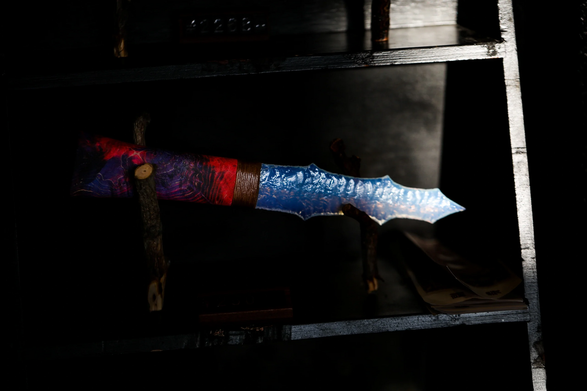 Red and blue handcrafted knapped display blades photographed in a dark workshop