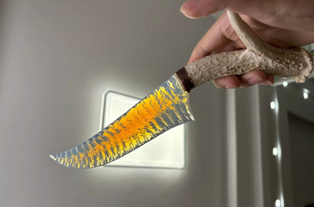 A maker holding a translucent yellow knapped blade beside a bright window